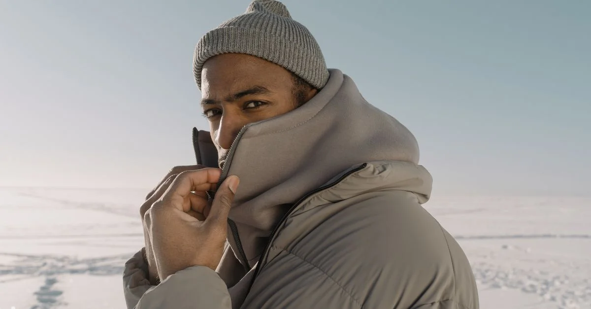 Un homme portant des vêtements d'hiver pose avec confiance dans un paysage enneigé, mettant en avant son style et sa chaleur.