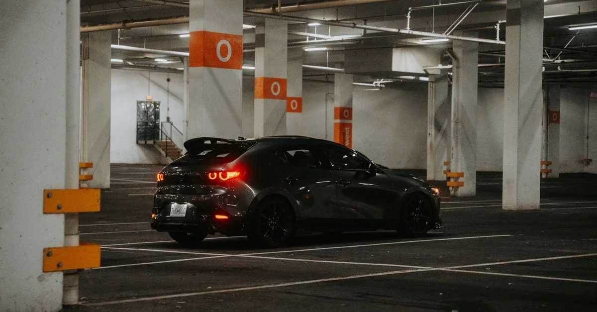 Une voiture noire moderne garée dans un garage souterrain faiblement éclairé, créant une atmosphère urbaine mélancolique.