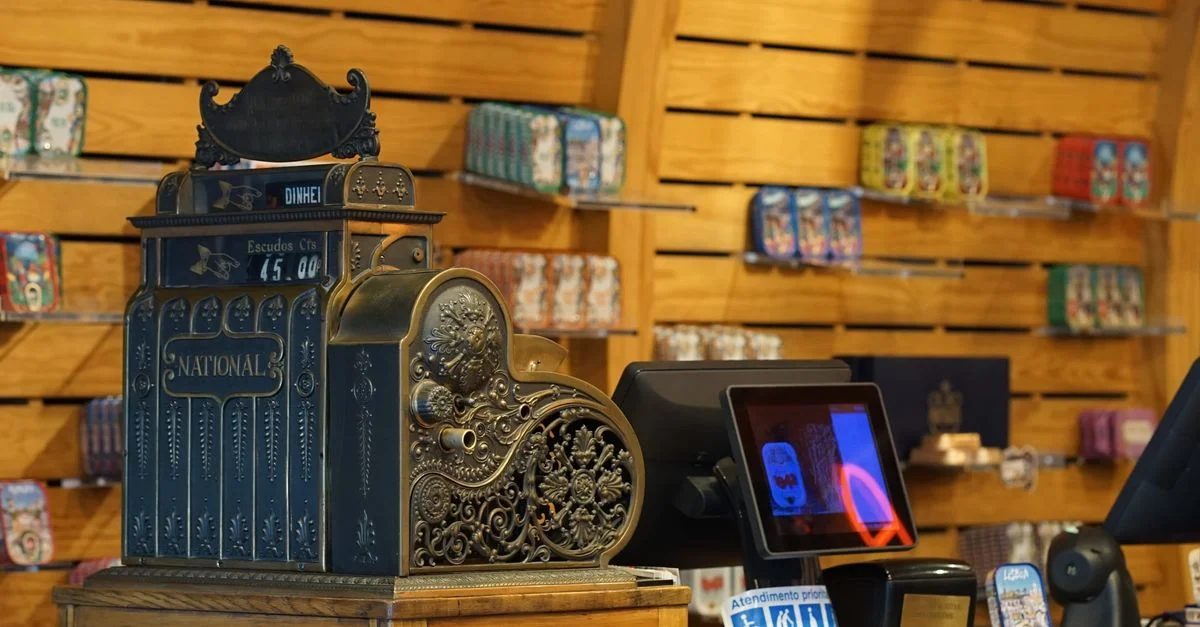 Caisse enregistreuse à l'ancienne exposée dans un magasin contemporain avec des systèmes de paiement modernes.