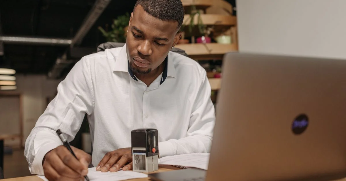 Un jeune homme en chemise blanche travaille avec assiduité à son bureau avec un ordinateur portable et des documents.