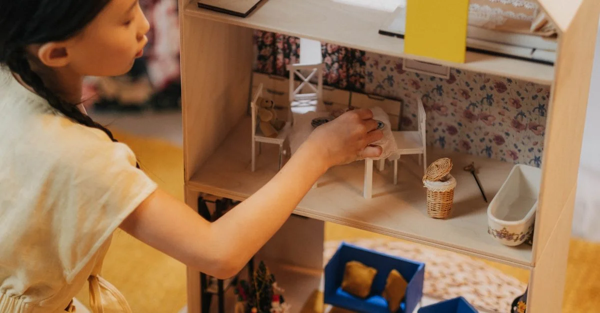 Une jeune fille jouant avec une maison de poupées à l'intérieur, illustrant l'imagination et le temps de jeu de l'enfance.