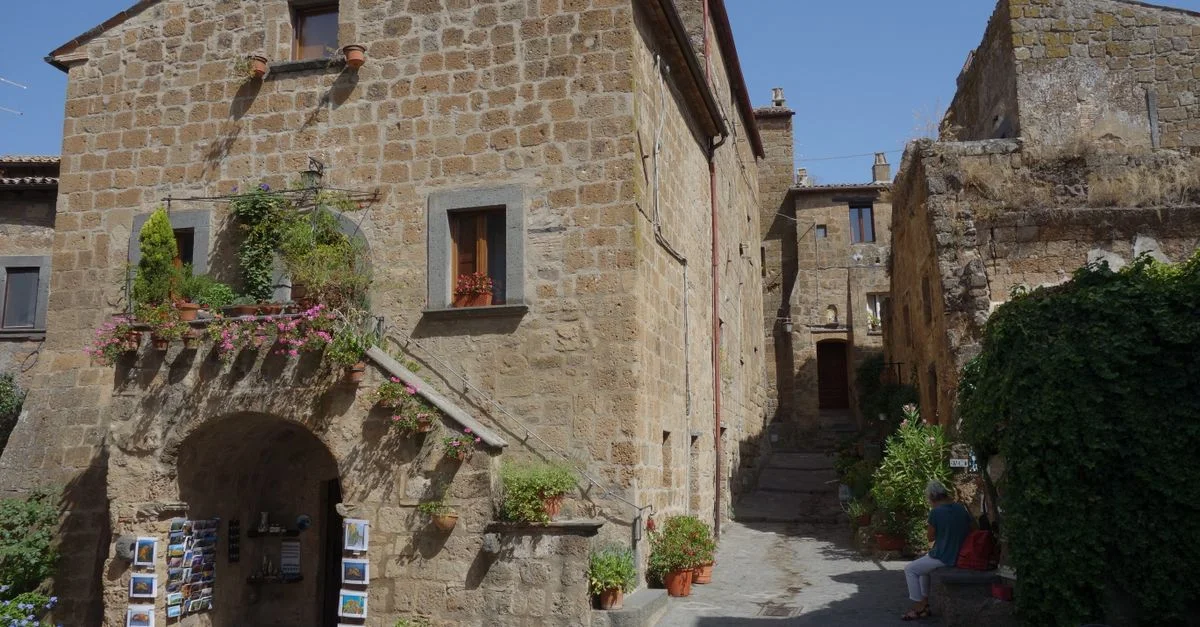 Bâtiment historique en pierre au charme rustique, entouré de fleurs colorées dans une ruelle italienne pittoresque.