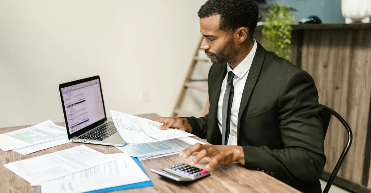 Un homme d'affaires en costume travaillant sur des documents et utilisant un ordinateur portable à un bureau.